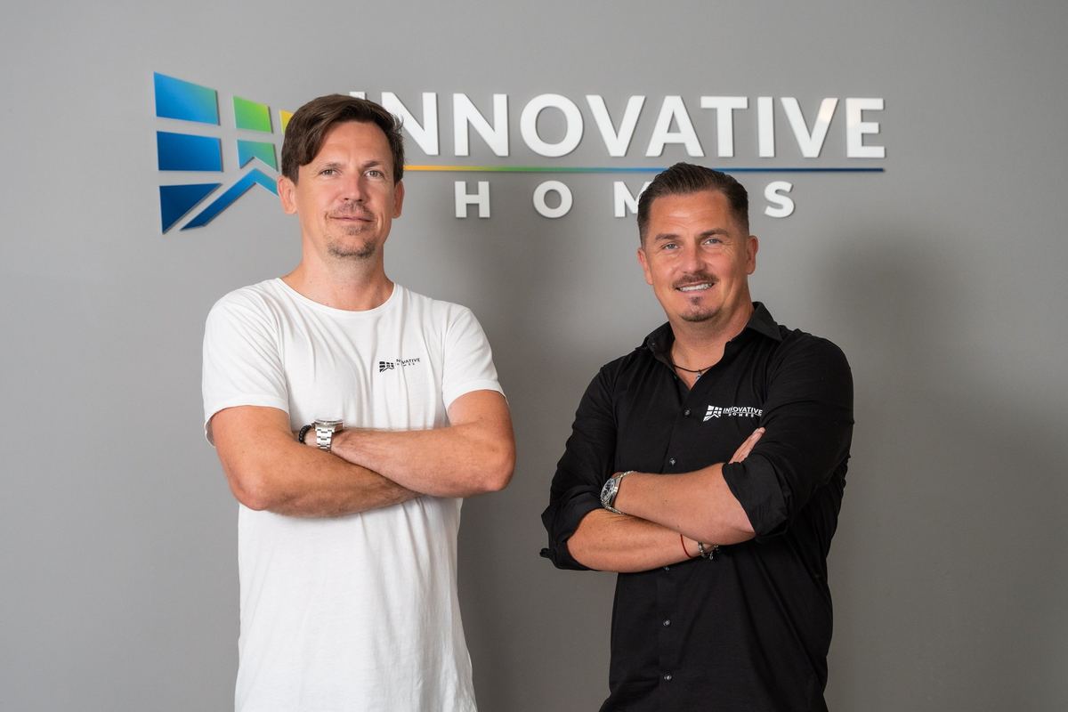 Waldemar Litau und Sebastian Marciniak, Geschäftsführer von Innovative Homes, vor der Logo-Wand im Büro
